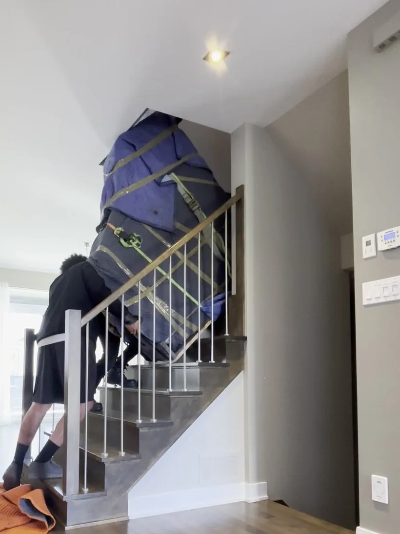 Un piano demi-queue, emballé et sanglé sur le côté, sort de l'étage et entre dans le virage de l'escalier